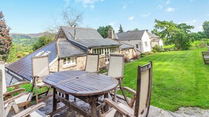 A stone house with a sloped roof, a patio with a round table and chairs, and a well-maintained lawn. - The Coach House - UK45027 (Crickhowell)