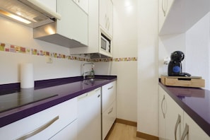 Une cuisine de taille réduite avec des meubles blancs, un plan de travail violet et un four à micro-ondes.