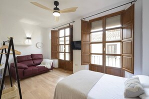 Une chambre à coucher avec un lit, un canapé rouge, des volets en bois, un ventilateur de plafond et un téléviseur.