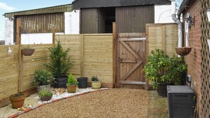 Een omheinde achtertuin met grind, potplanten en een houten poort.