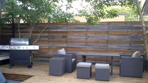 An outdoor patio with a grill, seating area, and a wooden deck.