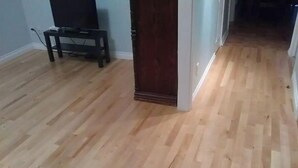 A room with wooden flooring, a dark wooden door, and a small table with a chair.