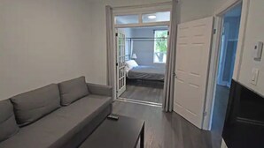 Een kamer met een bank, een klein tafeltje, een bed en een deur naar een andere kamer.
