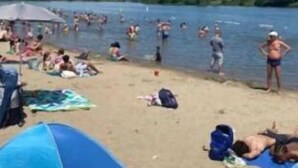 Een strand met mensen die zwemmen en zonnebaden, tenten, en een heldere lucht.