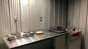 Une cuisine compacte dotée d’un plan de travail en acier inoxydable, d’une plaque de cuisson intégrée, d’un évier et d’un petit égouttoir à vaisselle.