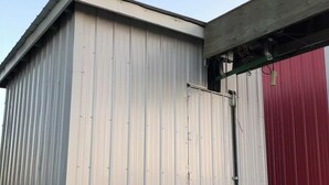 Il s’agit d’un bâtiment en métal dont la façade est peinte en blanc et en rouge, avec une grande porte et une petite fenêtre.