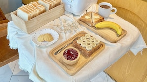 Mesa posta para o café da manhã com pão, manteiga, geleia, uma banana e uma xícara de café.