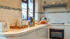 Et moderne køkken med hvide skabe, en indbygget ovn og et vindue med udsigt til grøn vegetation.