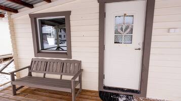 A wooden bench on a porch with a white door and a heart-shaped window decoration.