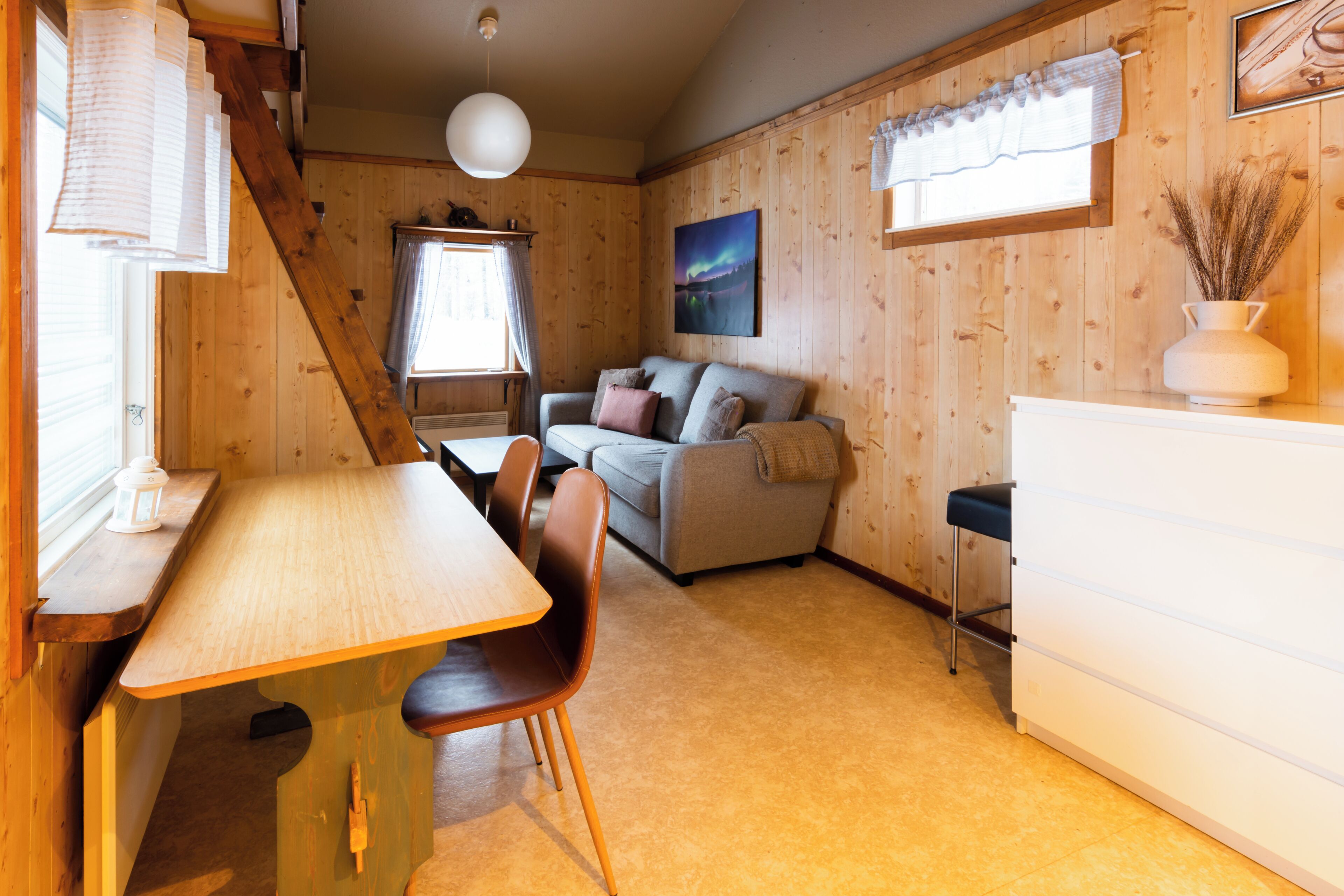 Un acogedor interior de cabaña con una mesa de comedor de madera, un sofá y un armario blanco.
