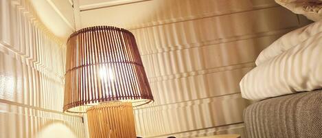 A bedside table with a lamp, a bed, and a wall with vertical lines.