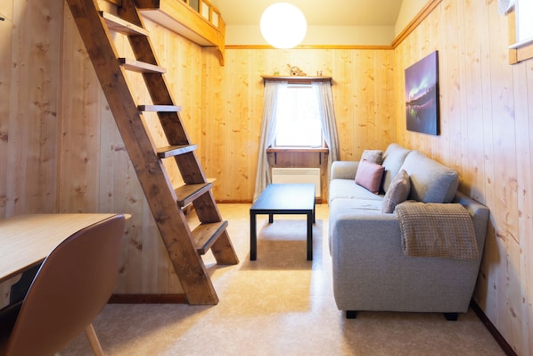 Un intérieur en bois comprenant un canapé, une table, une échelle et une fenêtre avec des rideaux.