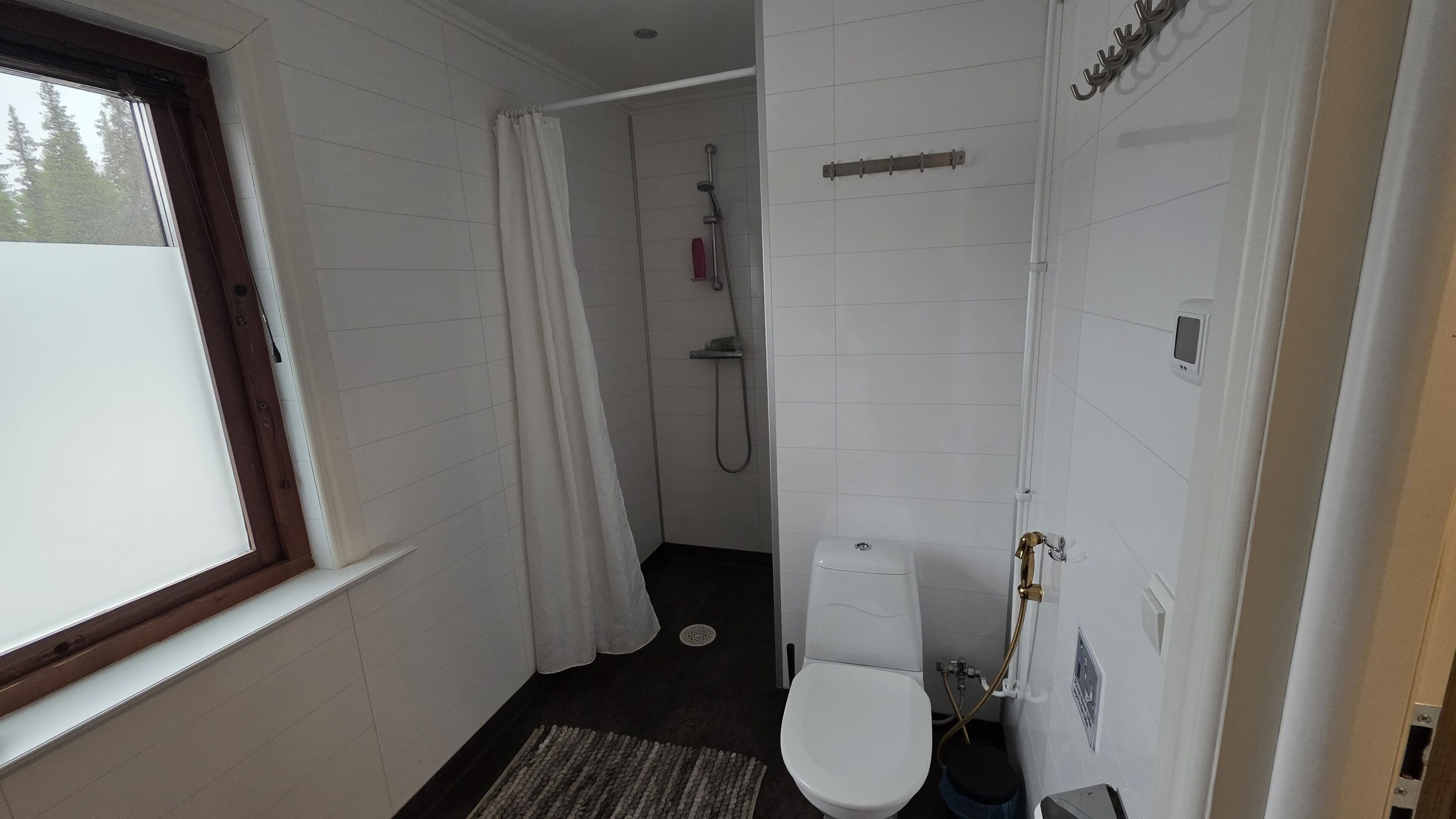 A small, compact bathroom with a toilet, a shower, and a window.