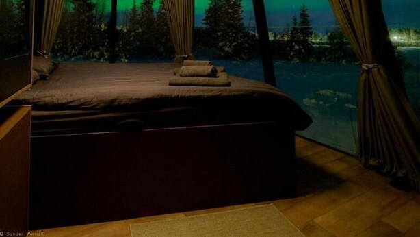 Una habitación con cama, cortinas y vistas a árboles y un cielo nocturno.