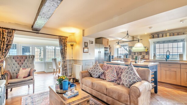 A spacious living area with a sofa, armchair, and a wooden coffee table. A kitchen is visible in the background with a large island and modern appliances. - 2 bedroom accommodation in Reedham (Reedham)