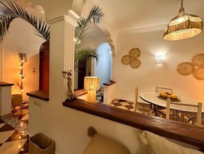 Un intérieur bien éclairé, avec un sol à carreaux, une table à manger ornée de fruits et une lampe suspendue.