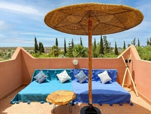 Une terrasse sur le toit, avec un lit, une table ronde en bois et un grand parasol.