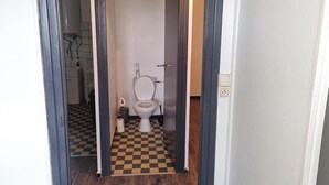 Un baño con inodoro, un rollo de papel higiénico y un cubo de basura pequeño.