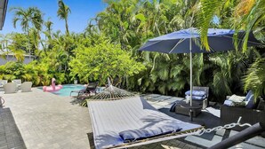A pool area with lounge chairs, a hammock, and a large umbrella. - Casa Coral with  Pool & Charcoal BBQ area (Miami)