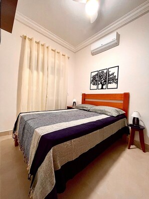 A neatly arranged bedroom with a bed, a nightstand, a lamp, and a wall-mounted air conditioner.