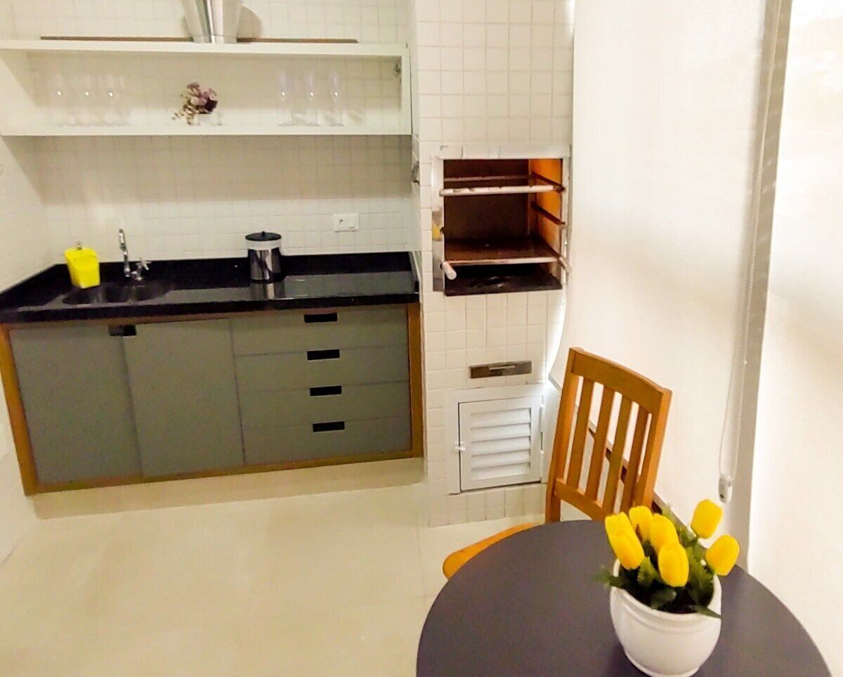 Une cuisine de taille réduite avec un plan de travail noir, un crédence carrelé blanc et une chaise en bois.