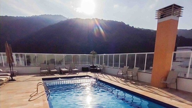 A pool area with a view of mountains, sun, and lounge chairs. - Apê Harmonia  (Ubatuba)