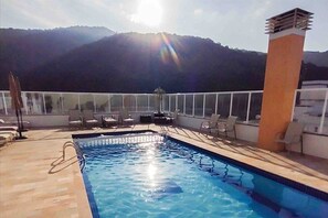 A pool area with a view of mountains, sun, and lounge chairs. - Apê Harmonia  (Ubatuba)