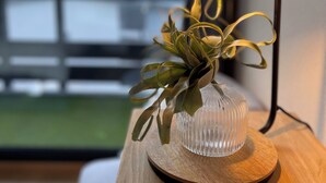 Una lámpara con base de madera y un florero de vidrio transparente que contiene una planta, colocada sobre una mesa de madera.