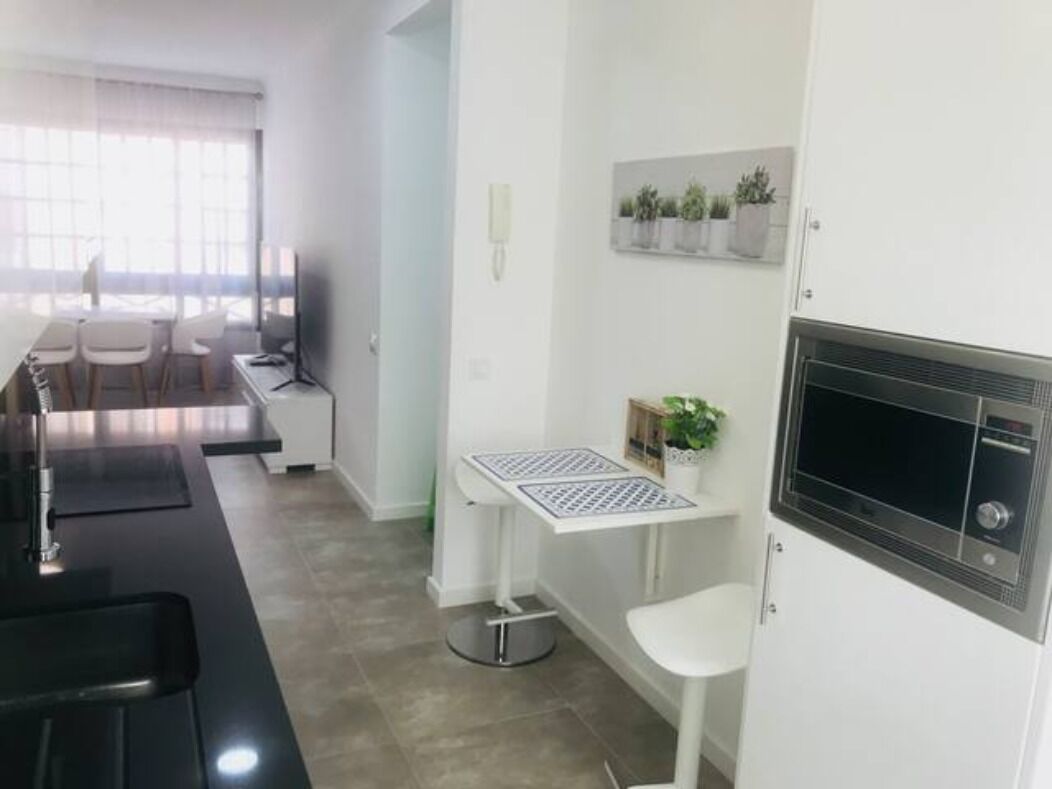 Une cuisine moderne avec un plan de travail noir, des armoires blanches et un four à micro-ondes encastré. On y trouve une petite table avec une plante en pot et une chaise blanche.