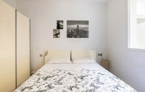 Quarto com cama, paredes brancas e três imagens em preto e branco de paisagens urbanas na parede.