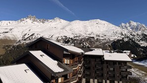 A mountain lodge with multiple wooden buildings, snow-covered roofs, and a backdrop of snow-capped peaks. - Apartment of 30m2 with 1 room, 1 bunk bed area and 1 living room with sofa (Les Allues)