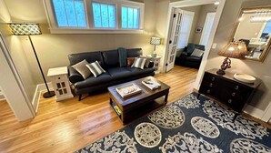 A living room with a black sofa, a coffee table, a patterned rug, and a lamp. - Capitol Charm in Dundee - East (Omaha)