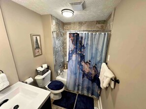 Une salle de bain avec un rideau de douche, des toilettes, un lavabo et un petit tableau encadré accroché au mur.
