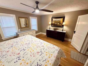Une chambre à coucher avec un lit, une commode, un ventilateur de plafond et un tableau accroché au mur.