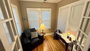 A room with a black leather sofa, a wooden table with a lamp, and a ceiling fan. - Capitol Charm in Dundee - East (Omaha)