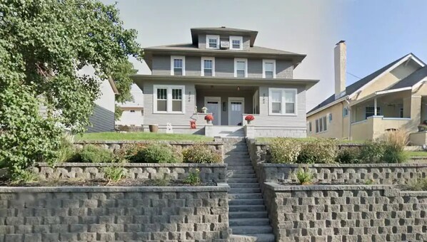 Une maison à deux étages avec un porche à l’avant, une cheminée et un escalier en pierre menant à l’entrée.