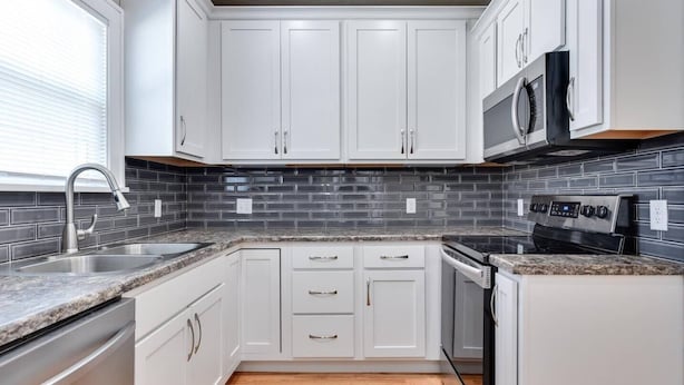 A kitchen with white cabinets, a granite countertop, a stainless steel sink, a microwave, and a stove. - Capitol Charm in Dundee - East (Omaha)
