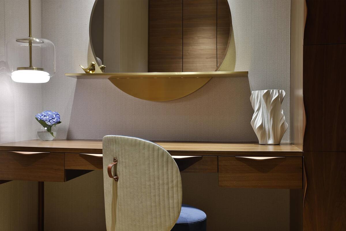 A modern bathroom with a wooden vanity, a round mirror, a gold accent, and a blue chair.