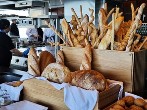 A variety of breads displayed in wooden baskets, with a kitchen area in the background. - Conrad Bahrain Financial Harbour (Manama)