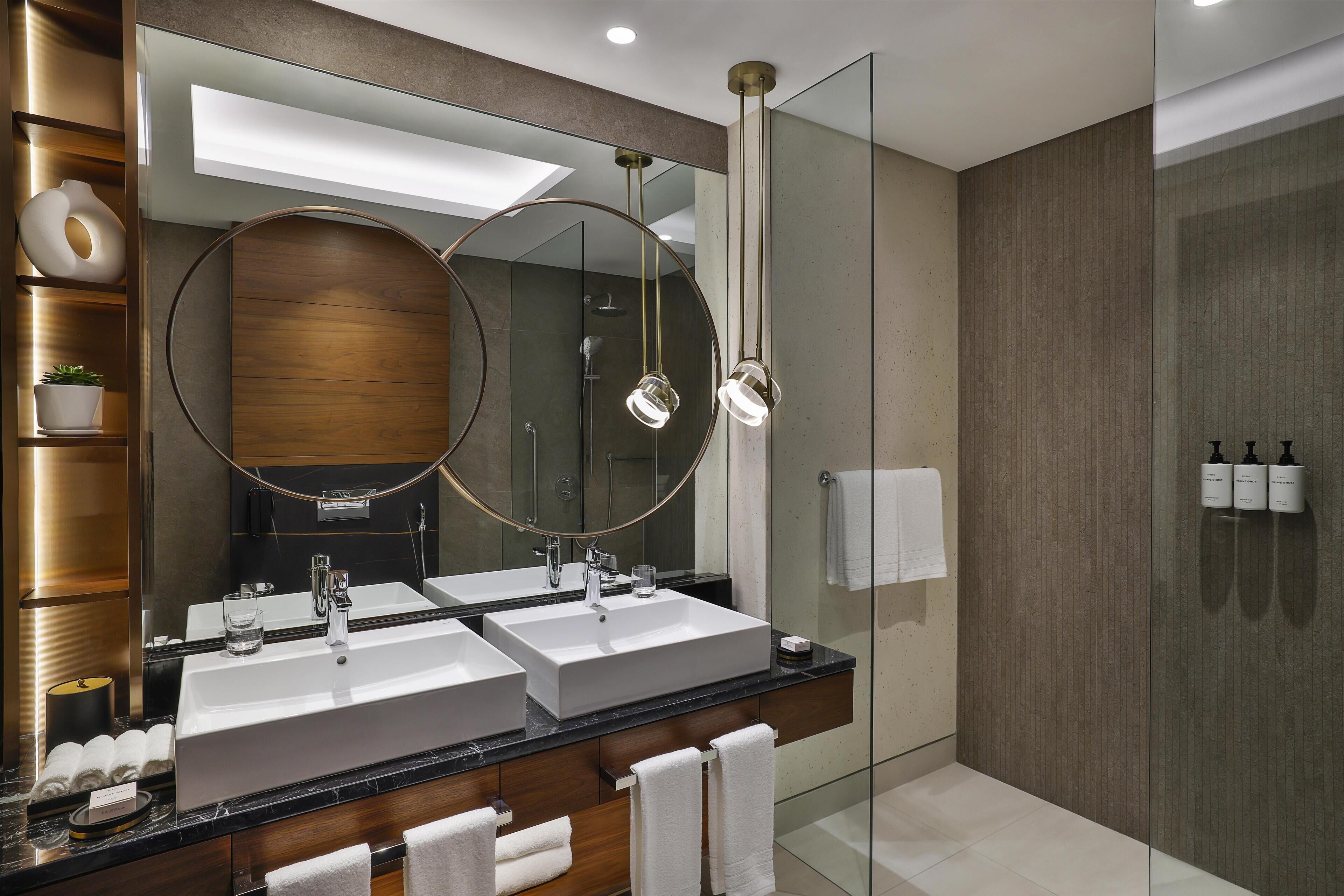 A modern bathroom with two sinks, a large mirror, and a glass-enclosed shower.