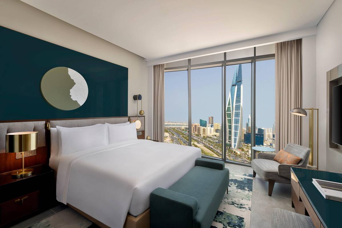 A hotel room with a large bed, a desk, a chair, and a view of a cityscape.