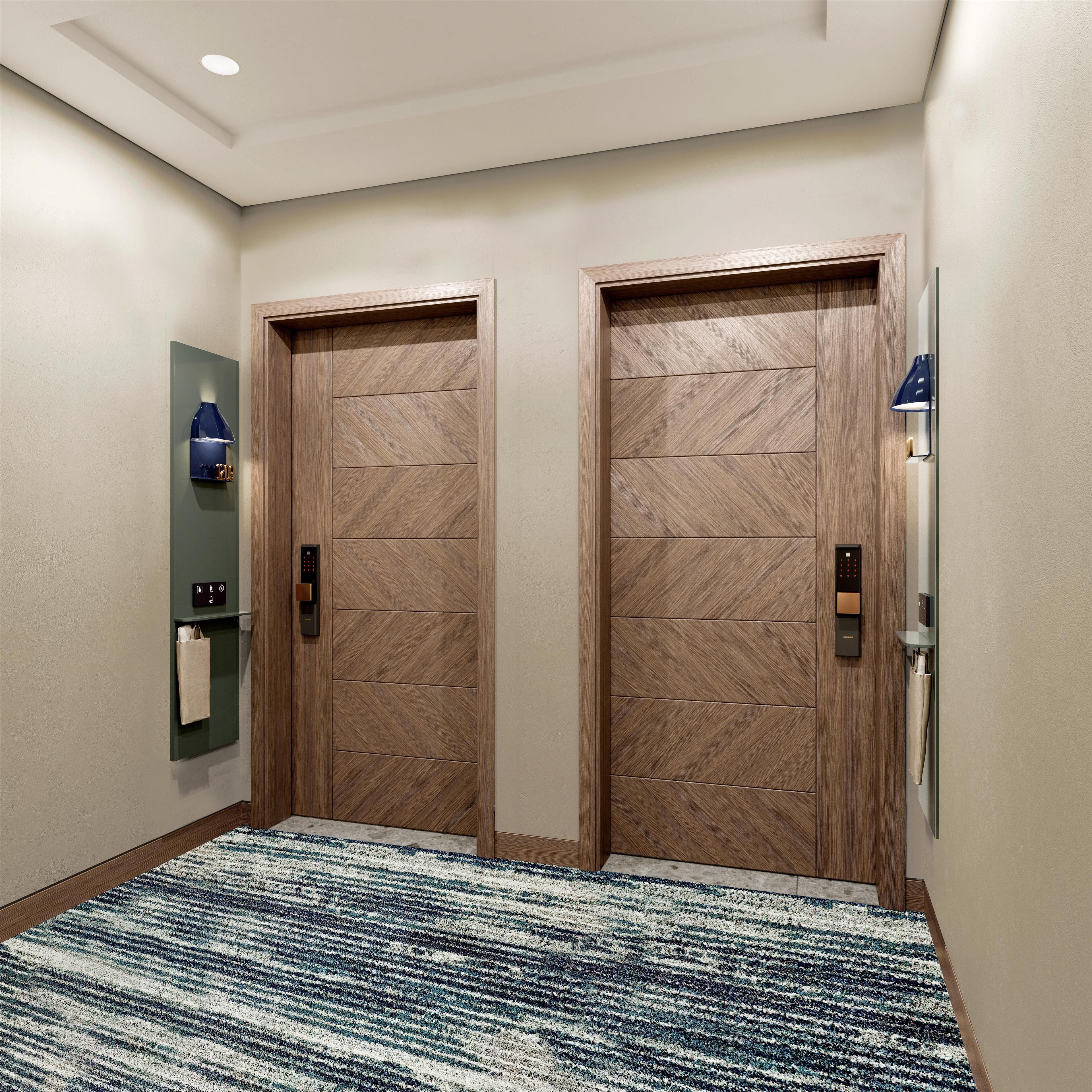 Un couloir avec deux portes en bois, une lampe bleue fixée au mur, un distributeur de serviettes et un tapis à motifs.