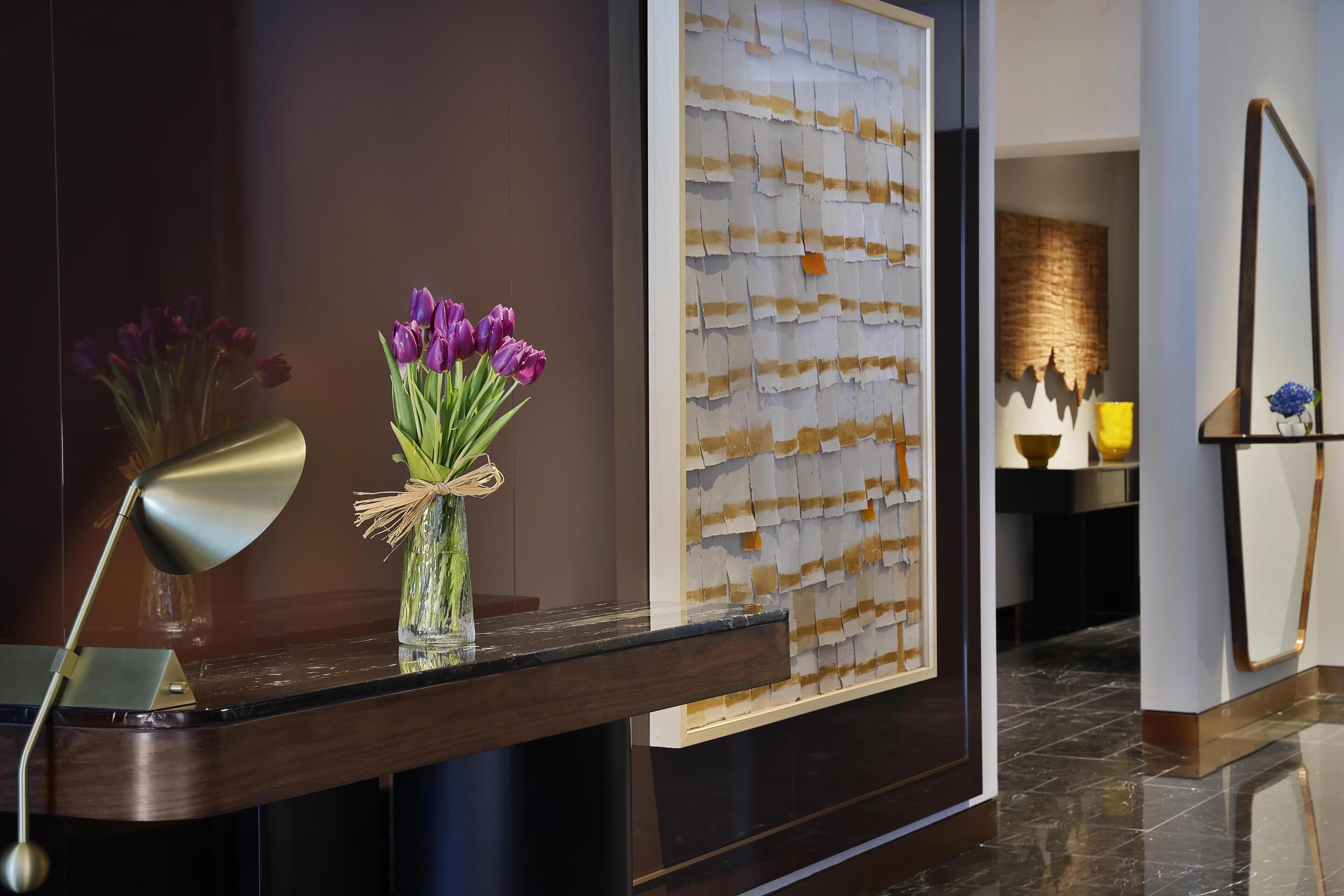 A reception area with a dark wood reception desk, a vase with purple flowers, and a wall with a textured pattern.