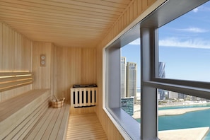 A modern room with wooden paneling, a wooden bench, a radiator, and a large window offering a view of a cityscape and coastline.