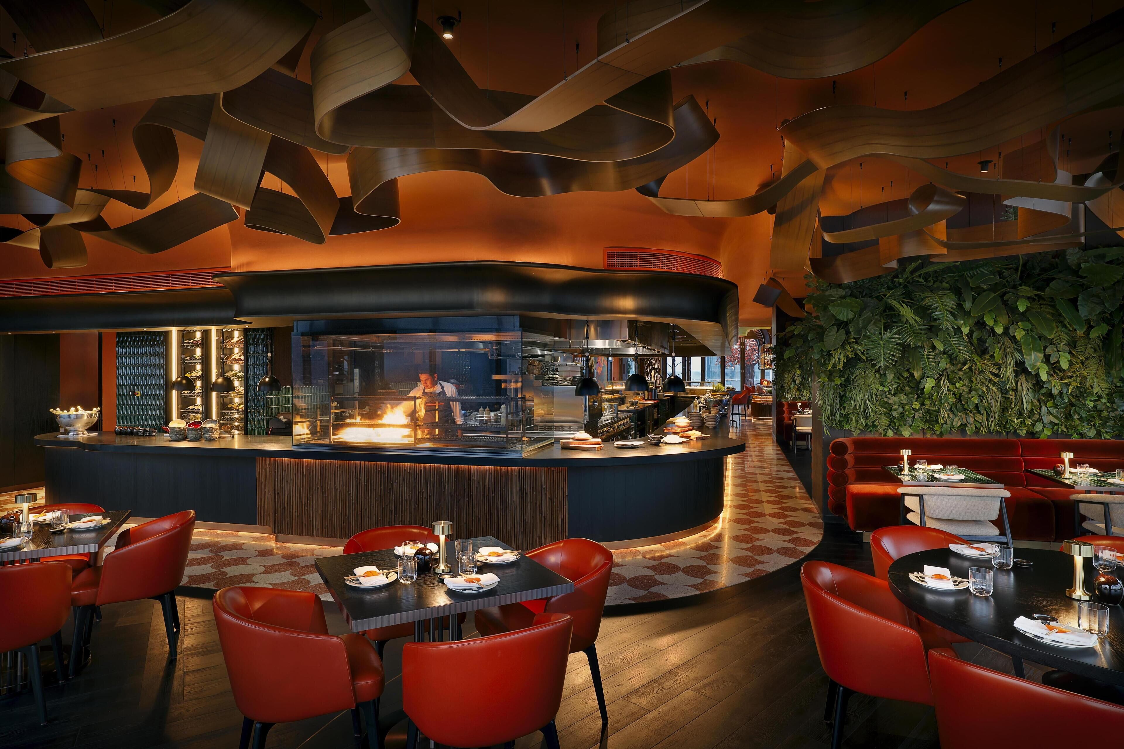 Un restaurante moderno con una barra curva, asientos rojos y un diseño de techo original.