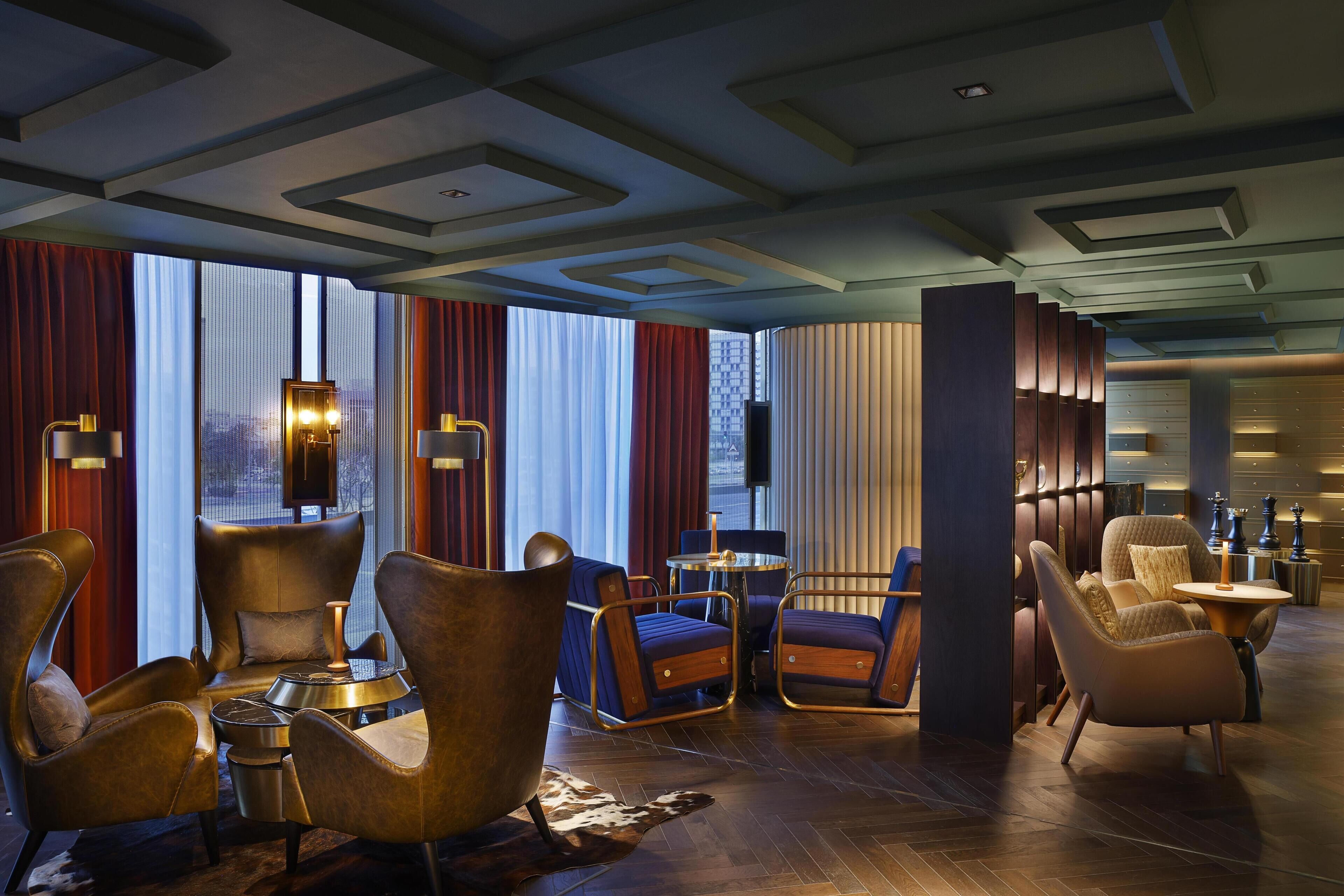 A modern lounge area with leather armchairs, a round table, and a large window with curtains.