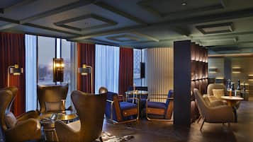 A modern lounge area with leather armchairs, a round table, and a large window with curtains.