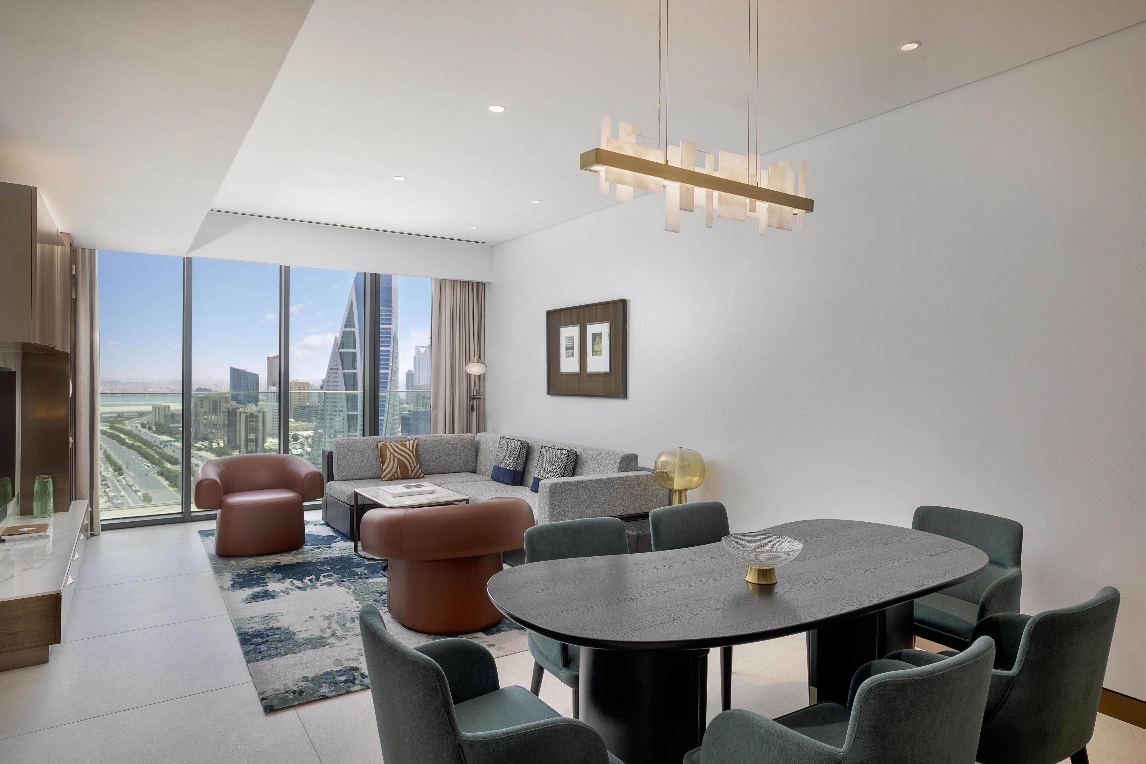 A modern living room with a round table, sofas, and a large window offering a city view.