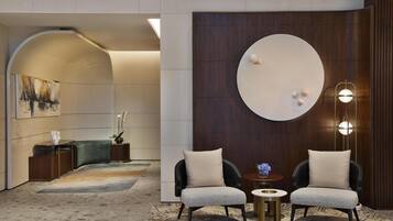 A modern lobby with a curved wall, a round mirror, two armchairs, a small table, and a decorative plant.