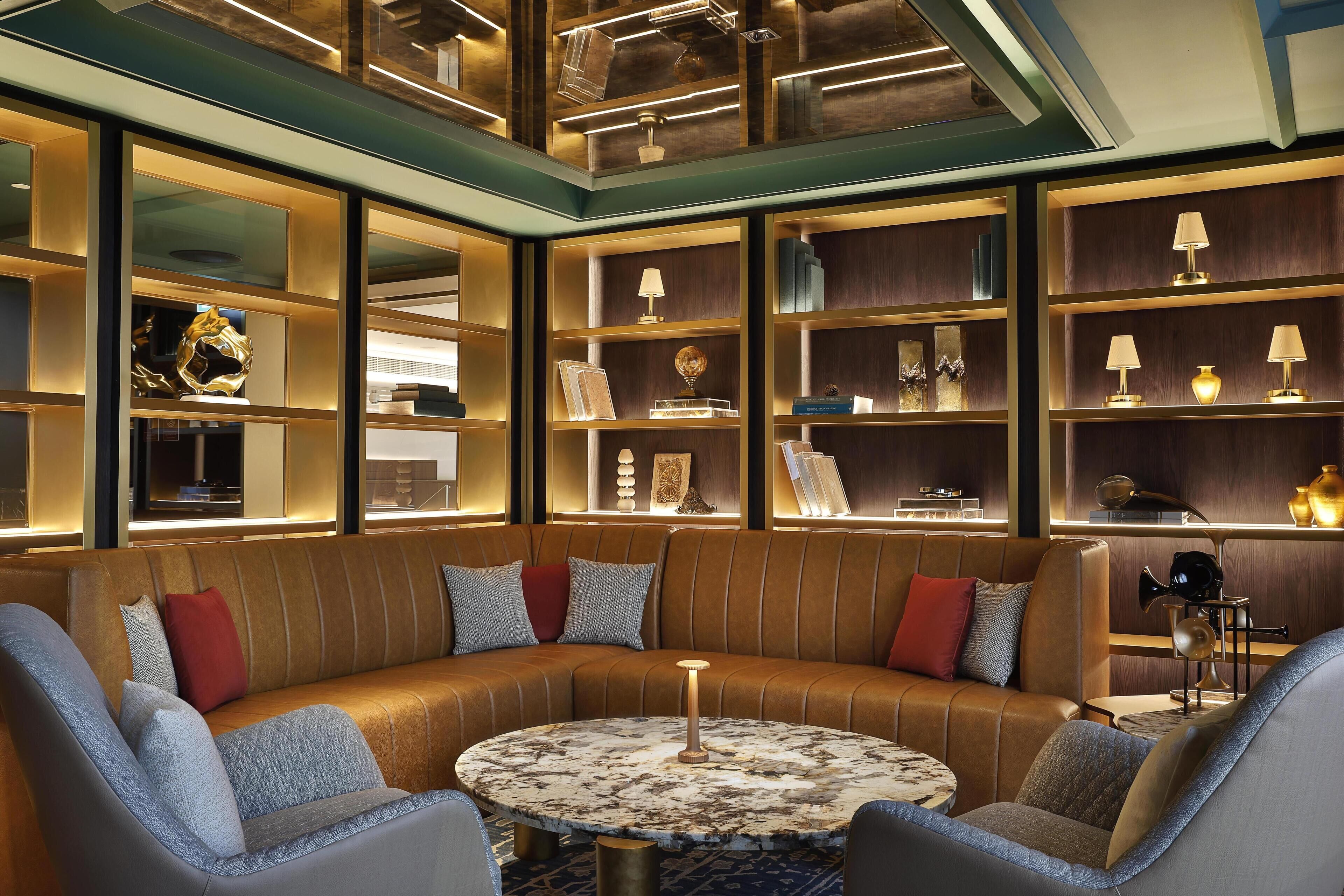 A modern lounge area with a leather sofa, round marble table, and shelves with decorative items.